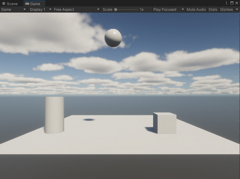 An image of the Game view. A cylinder and square sit on a plane, with a sphere lifted into the air between them.